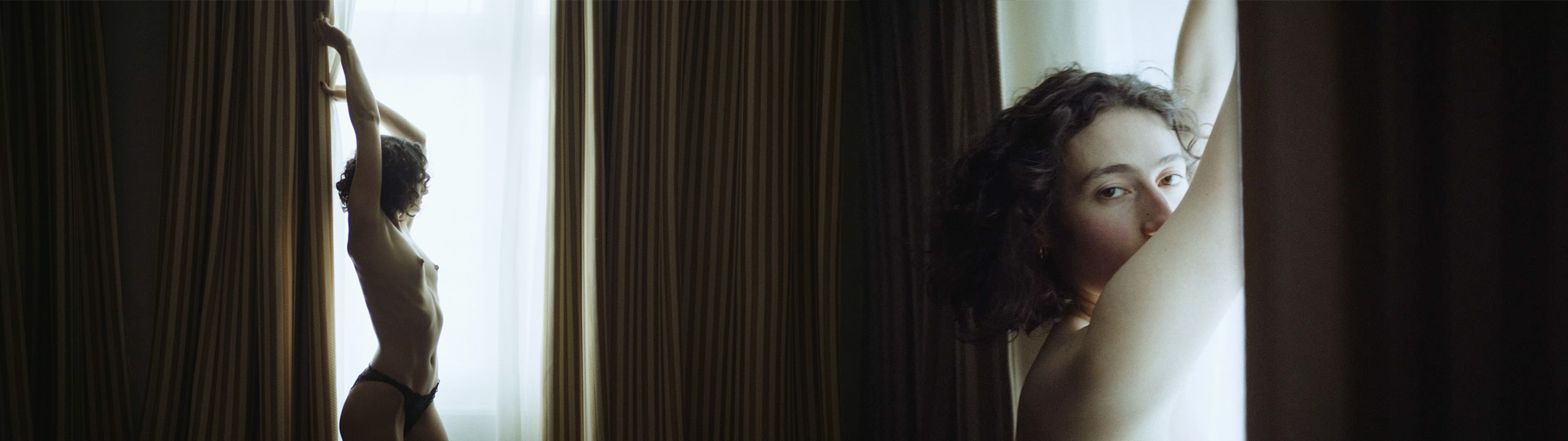 Left: Niki, wearing only panties, stands in backlight in front of a window with brownish curtains. Turning her gaze away from the camera, she stretches and holds the curtain with both hands. The lighting accentuates the contours and curves of her slender body. Right: Niki Blau in the same setting, this time only her head is visible. With her arms raised above her head, she gazes dreamily into the camera.